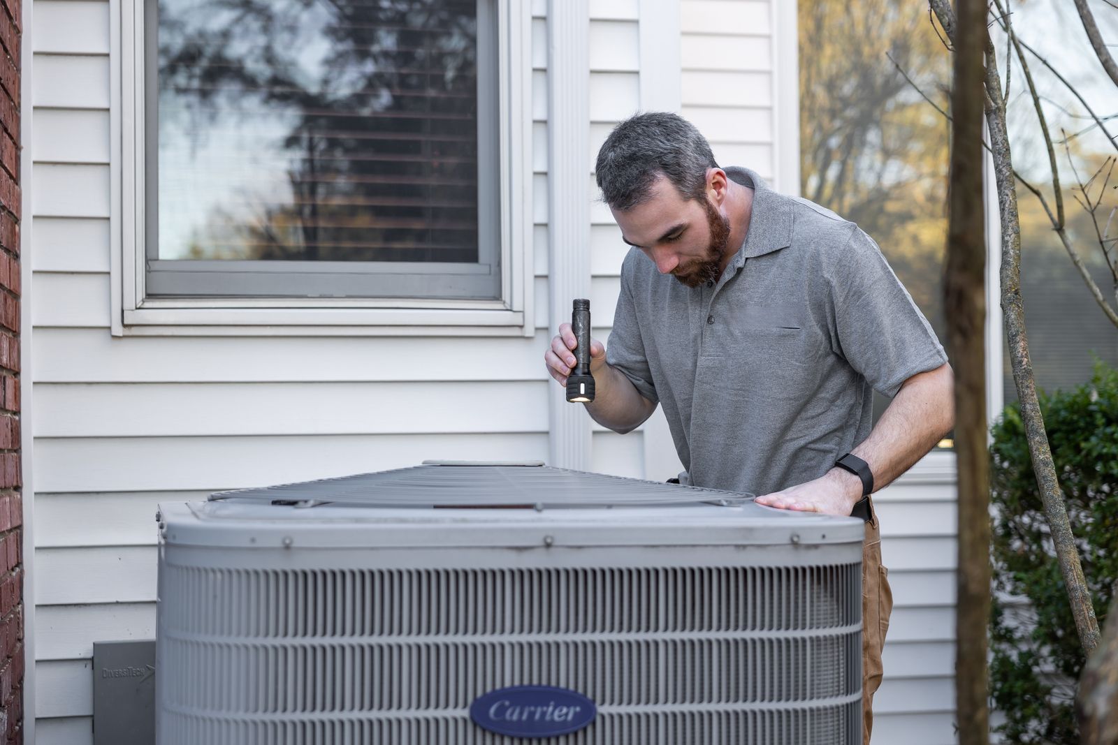 Technician inspecting an outdoor air conditioning unit beside a home during a maintenance visit